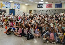 Students waving books in the air during an assembly.