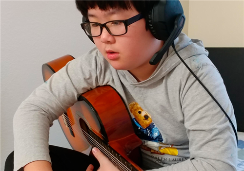 Elementary boy learns guitar in online music class